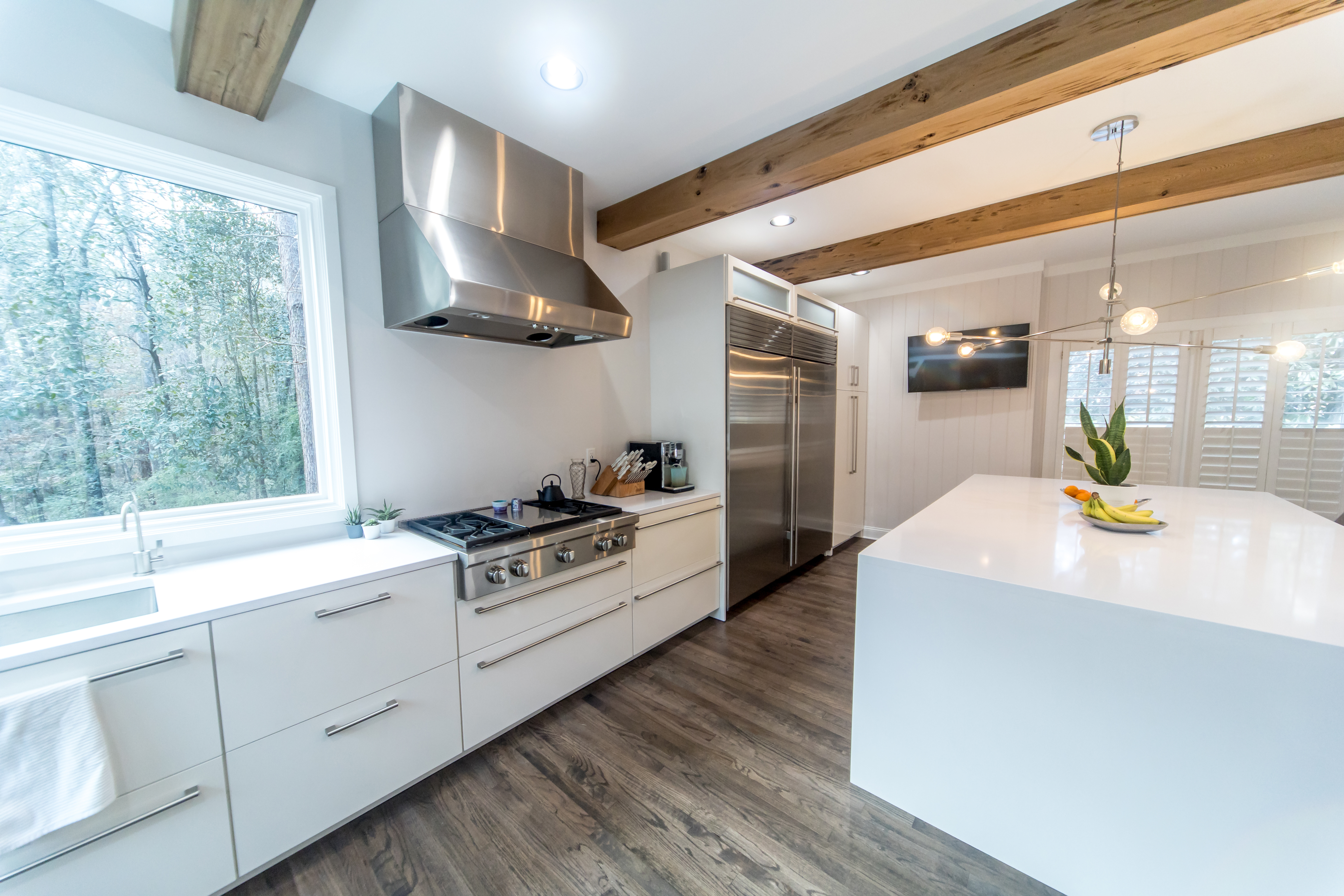 Modern kitchen with white cabinetry, stainless steel appliances, island countertop, and exposed wooden beams