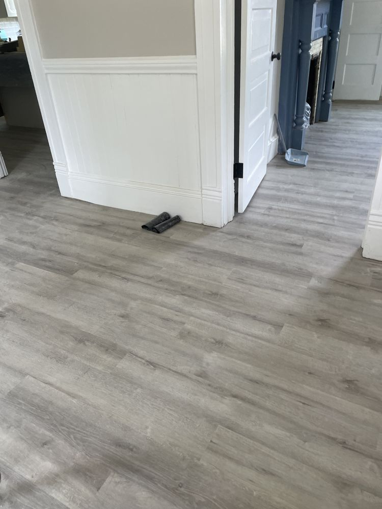 Gray wood-look vinyl plank flooring in modern hallway with white wainscoting and dark doors