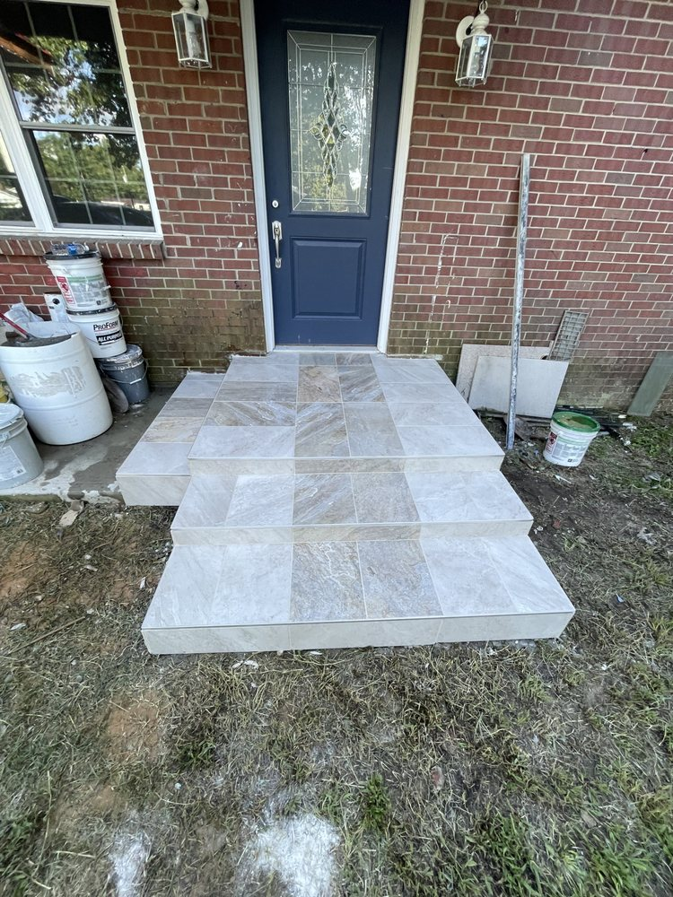 Outdoor tile display showing stone pavers laid on grass in front of brick home with blue door