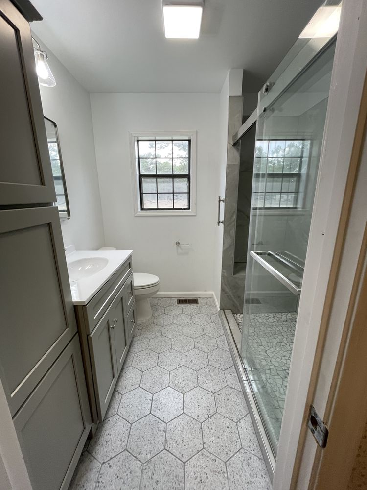 Modern bathroom with gray vanity, toilet, hexagonal floor tiles, and walk-in shower with glass doors