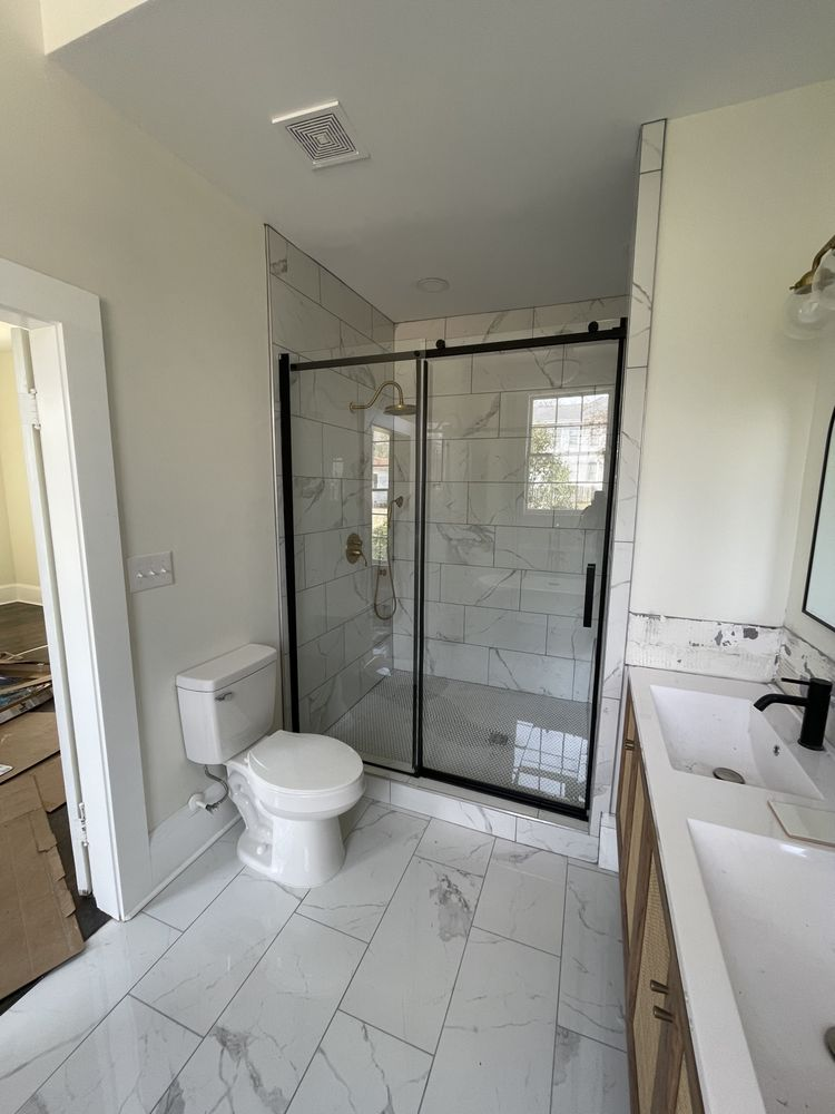 Modern bathroom with marble-look floor, glass shower enclosure with black frame, white toilet, and dual vanity sink
