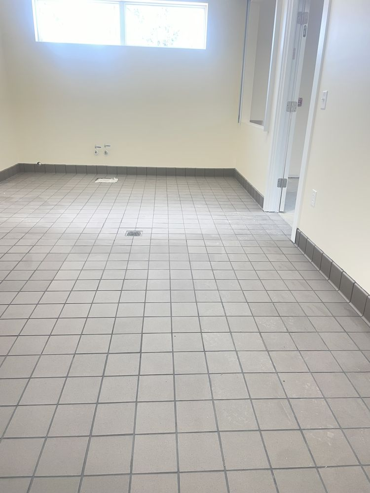 Empty room with gray tile flooring, beige walls, high window, and white door on right side