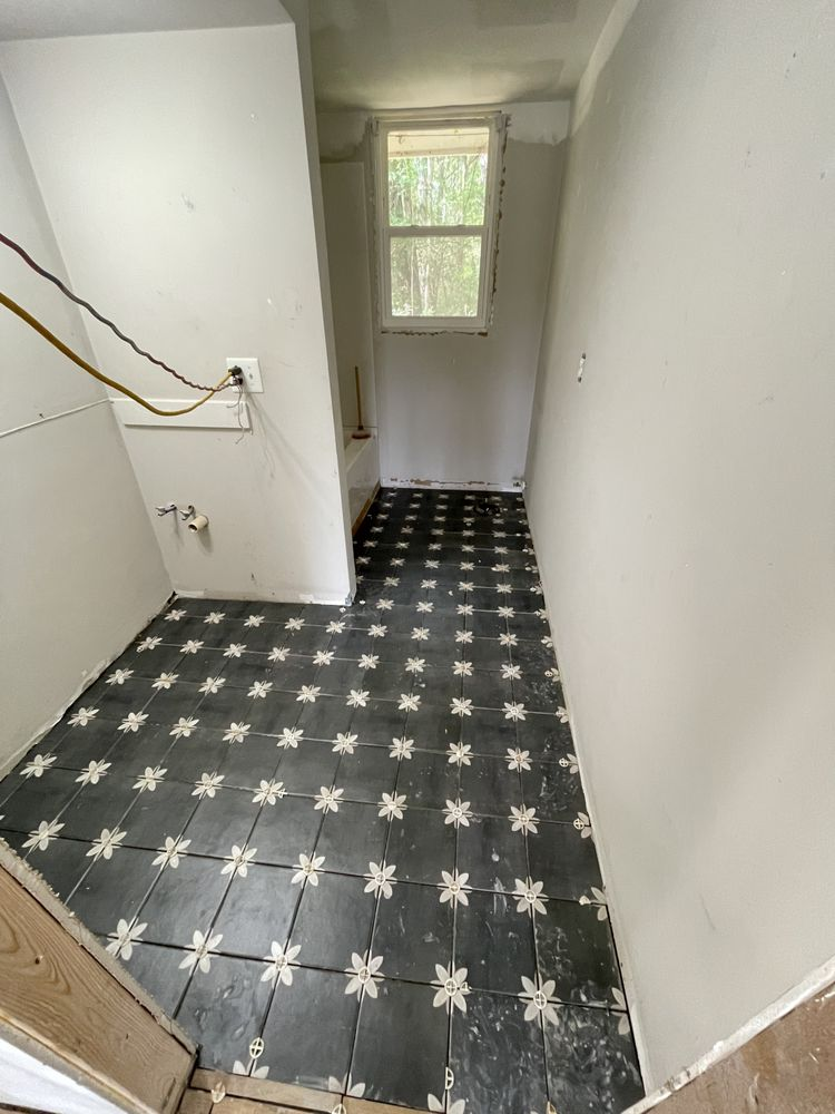 Narrow hallway with white walls, black and white star-patterned floor tiles, window at end, and electrical outlet on left wall