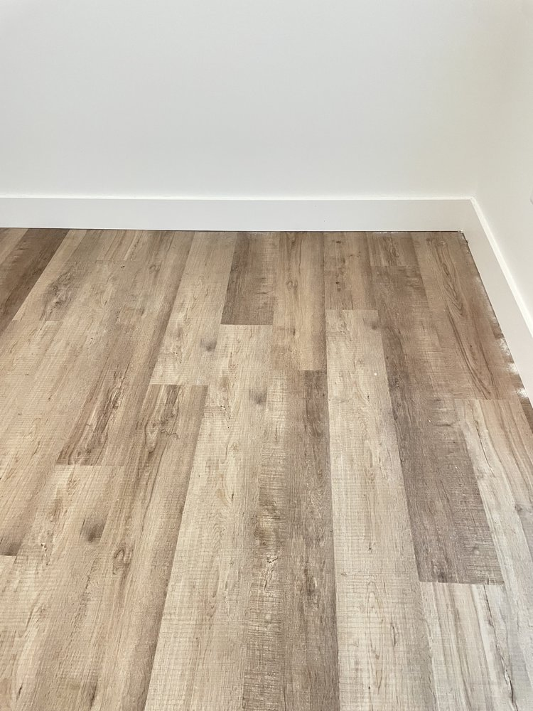 Newly installed light oak wood-look plank flooring in empty room with white baseboard trim