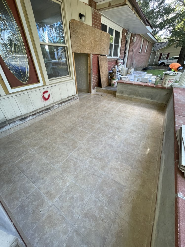 Newly installed tile flooring on a residential patio with construction materials and equipment visible in background