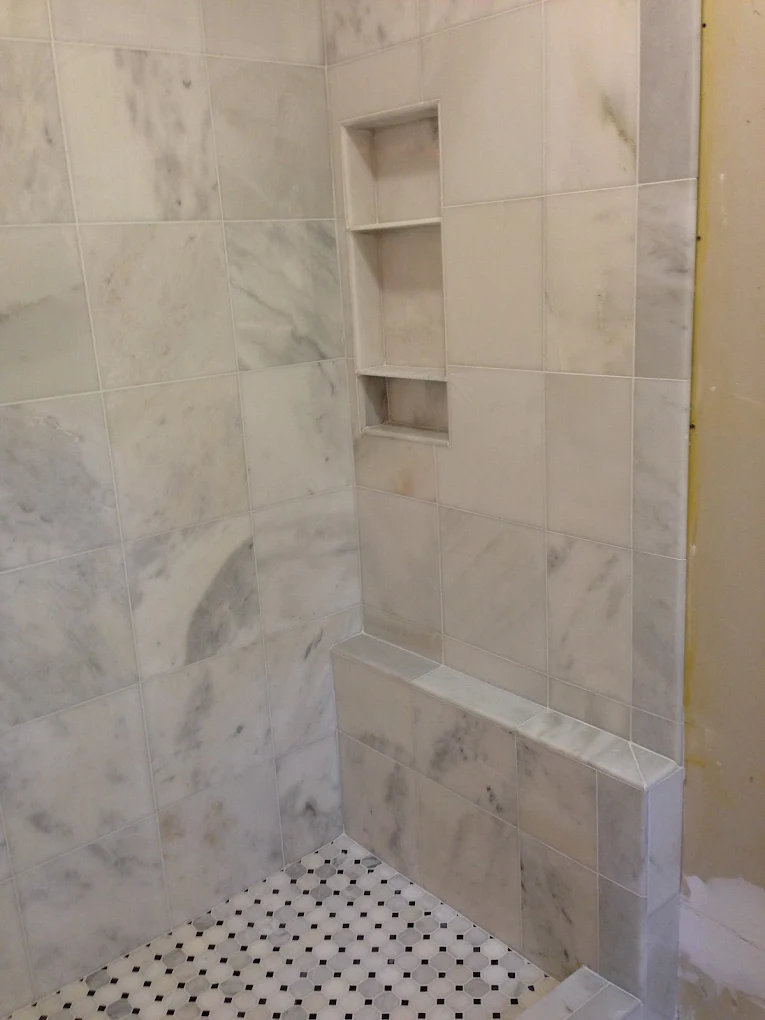 Marble tile shower stall with built-in shelving and mosaic tile floor