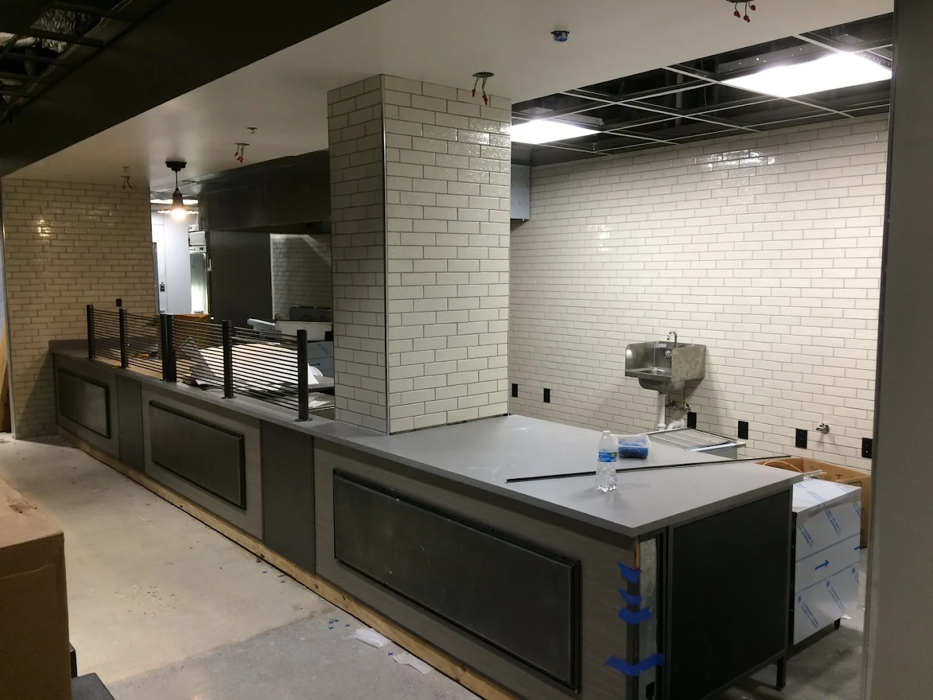 Modern commercial kitchen under construction with white subway tile walls and steel countertops